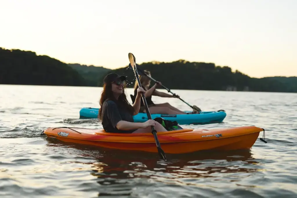 Two people paddling kayaks on a lake with hills in the background, labeled with the text "Kayaking".